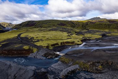 İzlanda 'nın Vik kenti yakınlarındaki toprak yolda, yeşil tepeler ve kıvrımlı nehir yatakları arasında Thakgil (Pakgil)' e giden yolda yalnız beyaz bir araba görülüyor.