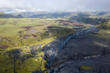 İzlanda 'nın Vik kenti yakınlarındaki Thakgil (Pakgil) yakınlarında yeşil tepeler ve kıvrımlı nehir yatakları arasında bulunan bir havza, seyrek bir yabanın hava aracı görüntüsüne sahiptir. Güzelliği ve yalnızlığı vurguluyorum.