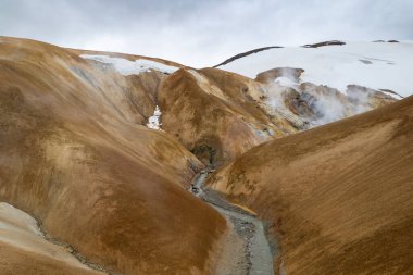 Çarpıcı bir hava aracı manzarası, İzlanda 'da çeşitli arazilerle çevrili dik ve sisli bir Kerlingarfjoll dağ yolunu gösteriyor.