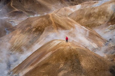 Çarpıcı hava aracı manzarası, çift yürüyüşçülerin İzlanda 'da çeşitli arazilerle çevrili dik ve sisli Kerlingarfjoll dağ yolunu gösteriyor.