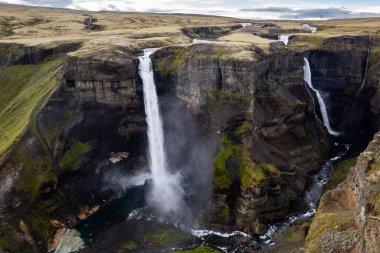 İzlanda 'daki güçlü Haifoss ve Granni şelalelerinin yemyeşil ve kayalık uçurumlarla çevrili derin bir kanyona aktığını gösteren nefes kesici bir hava aracı sahnesi.