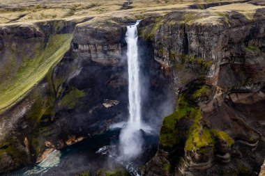 İzlanda 'daki güçlü Haifoss ve Granni şelalelerinin yemyeşil ve kayalık uçurumlarla çevrili derin bir kanyona aktığını gösteren nefes kesici bir hava aracı sahnesi.