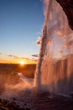 Gün batımı manzarayı aydınlatırken Seljalandsfoss şelalesinin düşüşü İzlanda 'daki Altın Çember' in canlı renklerle kaplı sisli bölgesiyle sakin ve nefes kesici bir doğal ortam yaratıyor.
