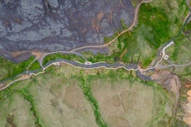 Drone aerial shot showcasing a Reykjadalur Hot Spring Thermal River in Iceland with vibrant valley with stream surrounded by rugged terrain and green fields. Perfect depiction of untouched wilderness clipart