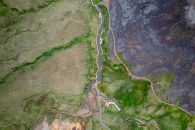 İnsansız hava aracı, İzlanda 'daki Reykjadalur Sıcak Bahar Termal Nehrinin engebeli arazi ve yeşil tarlalarla çevrili canlı vadisiyle görüntüsünü veriyor. Dokunulmamış vahşi doğanın mükemmel tasviri