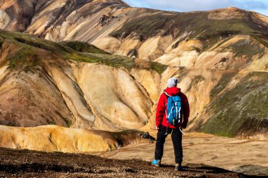 Canlı bir dağda, renkli tepeler ve dramatik manzaralarla çevrili Landmannalaugar 'ı tek başına ayakta tutan yürüyüşçü. Sahne macera, yalnızlık ve vahşi doğayla bağlantı hissi uyandırıyor.