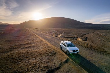 Dolambaçlı bir yolda, doğayla ve dağlarla çevrili güzel bir günbatımı boyunca bir araç. Seyahet, keşif ve sakin kırsal yaşamı tasvir eden sakin ve huzurlu manzaranın havadan görünüşü