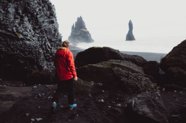 Atlantik Okyanusu 'nun dalgaları ve volkanik kaya oluşumlarıyla İzlanda' nın Altın Çember bölgesindeki VİK Myrdal 'ın kayalık arazisi ve Reynisfjara plajı boyunca ayakta duran bir kişi.
