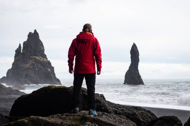 Atlantik Okyanusu 'nun dalgaları ve volkanik kaya oluşumlarıyla İzlanda' nın Altın Çember bölgesindeki VİK Myrdal 'ın kayalık arazisi ve Reynisfjara plajı boyunca ayakta duran bir kişi.