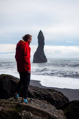 Atlantik Okyanusu 'nun dalgaları ve volkanik kaya oluşumlarıyla İzlanda' nın Altın Çember bölgesindeki VİK Myrdal 'ın kayalık arazisi ve Reynisfjara plajı boyunca ayakta duran bir kişi.