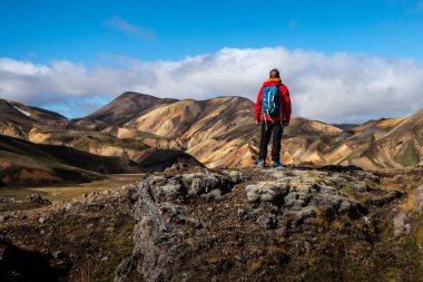 Canlı bir dağda, renkli tepeler ve dramatik manzaralarla çevrili Landmannalaugar 'ı tek başına ayakta tutan yürüyüşçü. Sahne macera, yalnızlık ve vahşi doğayla bağlantı hissi uyandırıyor.
