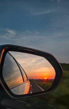 Dikiz aynasında güzel bir gün batımı, otoyolda hızlı bir araba yolculuğu. Açık yaz gökyüzü. 