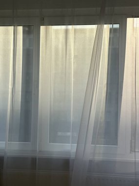 Saf beyaz perdeleri olan yumuşak bir pencerenin yakın görüntüsü yayılmış güneş ışığının filtrelemesine olanak sağlıyor. Narin kumaş havadar ve sakin bir hava yaratır.