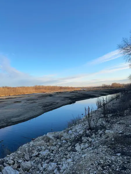 Dar, sakin bir nehir kayalık bir kış manzarasında akar ve açık mavi gökyüzünü mükemmel bir şekilde yansıtır. Çıplak ağaçlar ve kuru bitki örtüsü. Yumuşak sabah ışığı altında kıyılar.