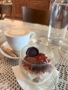 Bir fincan kapuçino ve üzerinde çikolatalı trüf mantarı olan lezzetli bir bardak tiramisu ile sıcacık bir kafe anı. Rahatlamış bir öğleden sonra ve hoş bir hoşgörü için mükemmel bir ortam..