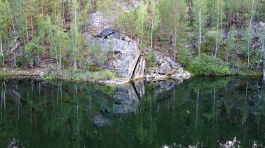 Fotoğrafta üzerinde kayalar ve ağaçlar olan bir göl var.
