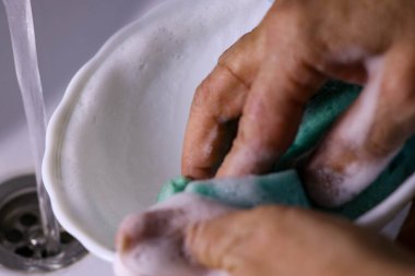 Görüntü, tabağı süngerle temizleyen bir kızı gösteriyor.