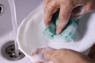 Fotoğrafta bir kız tabağı süngerle yıkarken görülüyor.