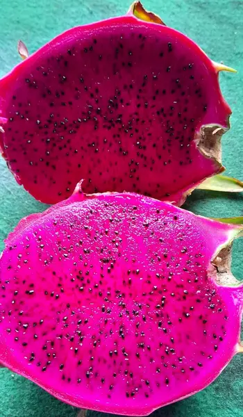 Dilimlenmiş, canlı pembe ejderha meyvelerinin yakın plan görüntüsü zıt yeşil bir zeminde siyah tohumları gösteriyor, taze ve tropikal özlerini yakalıyor..