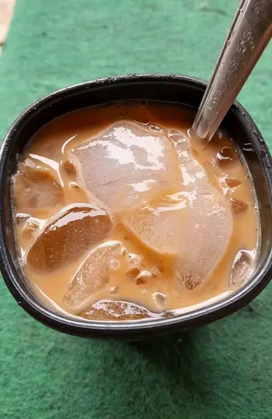 Serinletici buzlu kahve, siyah bir fincanda soğutulmuş, desenli yeşil arka planda kremalı süt ve buz küpleri sunuluyor..