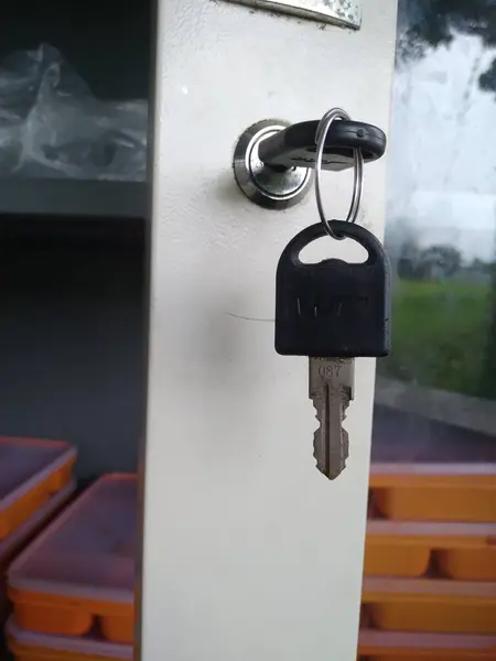 Beyaz bir yüzeydeki kilitten sarkan anahtarın yakın plan çekimi. Anahtar gümüş yüzüklü siyah ve üzerinde 