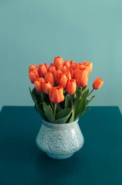 Mavi bir masanın üzerinde mavi bir vazoda mavi bir duvara karşı duran turuncu laleler. Parlak renk zıtlıkları. İç mekanda minimalizm