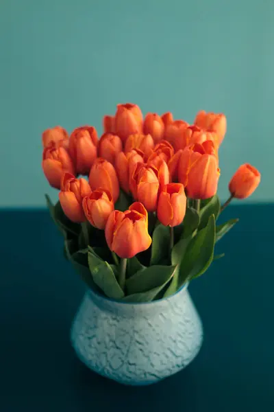 Mavi bir masanın üzerinde mavi bir vazoda mavi bir duvara karşı duran turuncu laleler. Parlak renk zıtlıkları. İç mekanda minimalizm