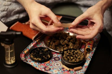 Bir esrarı dikkatlice sarmak için esrarı renkli bir tepsinin üzerinde sarmak. Sahnede bir öğütücü, bir kese ve dingin ve odaklanmış bir sigara piposu var.