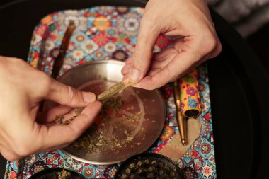 Bir esrarı dikkatlice sarmak için esrarı renkli bir tepsinin üzerinde sarmak. Sahnede bir öğütücü, bir kese ve dingin ve odaklanmış bir sigara piposu var.