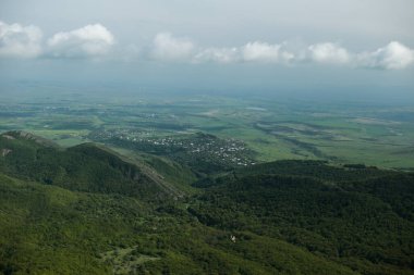 Önünde kayalık bir uçurum ve dalgalı yeşil tepeleri olan dramatik bir dağ manzarası uzaklarda sise dönüşüyor. Zengin dokular ve doğal katmanlar derinlik ve uçsuz bucaksızlık hissi yaratır..