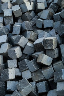 Görünür doku ve doğal kusurlarla dolu, asfalt döşeme için kullanılan, sıkıca paketlenmiş gri taş küpler. Yumuşak gün ışığında çekilen, yapının ve yüzeysel detayların vurgulandığı.