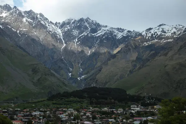 Gürcistan 'daki Kafkasya Dağları' nın eteklerine kurulmuş, karlı tepeleri, dramatik tepeleri ve dağınık bulutları olan bir dağ kasabasının manzarası..