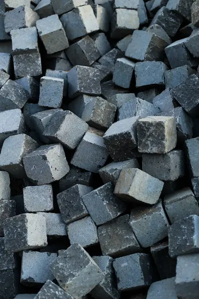 Görünür doku ve doğal kusurlarla dolu, asfalt döşeme için kullanılan, sıkıca paketlenmiş gri taş küpler. Yumuşak gün ışığında çekilen, yapının ve yüzeysel detayların vurgulandığı.