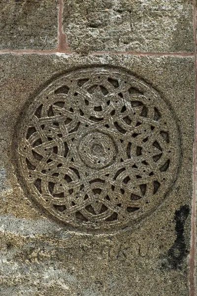 Muhtemelen tarihi mimari veya dini mekanlardan gelen simetrik iç içe geçmiş bir deseni olan dairesel bir taş oymanın ayrıntılı görüntüsü. Doku ve işçilik açıkça görülüyor..