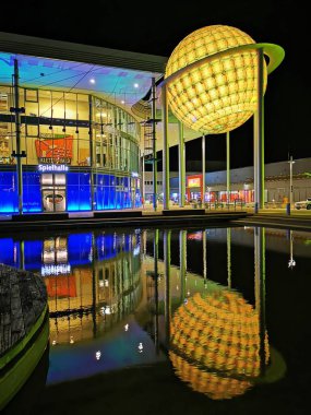 Leipzig, Almanya - 26 Şubat 2022: Suya yansıyan parlak ışıklı modern bir bina. Ön planda, küresel bir yapı görülebilir, içeriden aydınlatılır.