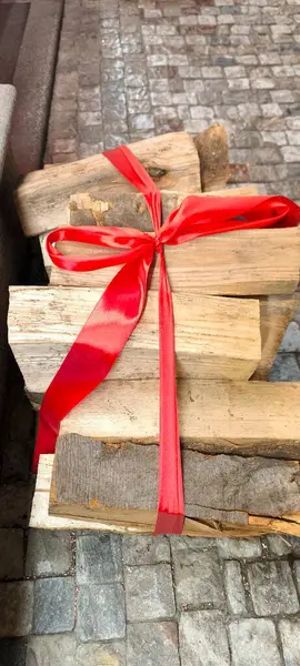 Düzgün istiflenmiş odun, parlak kırmızı bir kurdele ile bağlanmış, hediye olarak hazırlanmış, kullanıma hazır görünüyor, sıcaklığı ve rahatlığı simgeliyor. Yüksek kaliteli fotoğraf