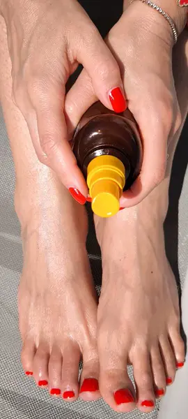 Kırmızı pedikür ve manikürlü, bronzlaşma yağı şişesi tutan iyi bakımlı kadınlar.