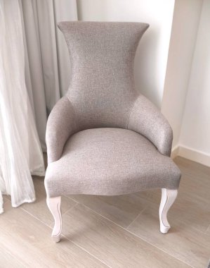 Zarif gri bergera kanat sandalyesinin yakın çekimi açık perdelere karşı duruyor.