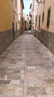 Alcudia, İspanya - 11 Nisan 2025: Alcudia İspanya 'nın eski kesiminde pencereli ve balkonlu eski binalar arasında dar bir kaldırım manzarası