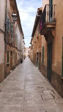 Alcudia, İspanya - 11 Nisan 2025: Alcudia İspanya 'nın eski kesiminde pencereli ve balkonlu eski binalar arasında dar bir kaldırım manzarası