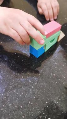 Masanın parlak pürüzsüz yüzeyinde renkli ahşap küplerle oynayan küçük çocuk elleri