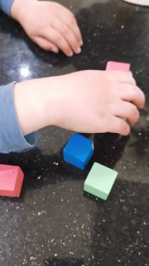 Masanın parlak pürüzsüz yüzeyinde renkli ahşap küplerle oynayan küçük çocuk elleri