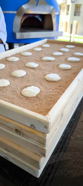Ahşap bir kutunun içindeki un yatağında geleneksel ahşap fırının arka planına karşı düzgünce yerleştirilmiş yuvarlak hamur somunları.