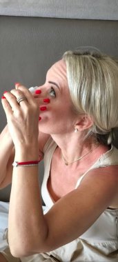 Parlak manikürlü kadınların yakın çekimi şişeden gözlerine damla damlatıyor.