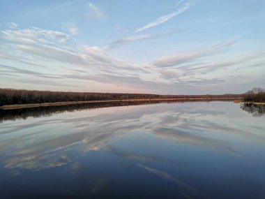 Gün batımında nehrin sessiz yüzeyinde yansıyan aynadaki gibi pembe renkli ve ufuk çizgisi olan bulutlu sakin bir gökyüzü.