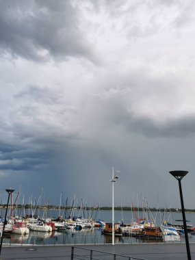Sakin bir limanda, bulutlu bir günde, gök gürültülü bir fırtına vadeden bir sürü demirlemiş yat ve yelkenli gemi.