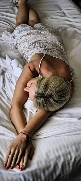 Sarı saçlı kadın, dantelli geceliğiyle beyaz çarşafa uzanıyor. Rahatlama, dinlenme, zevk, rahatlama ve uyku gösteriyor.