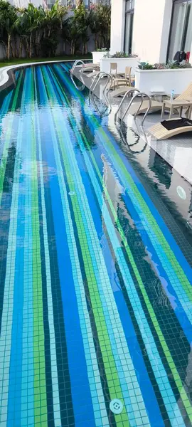 Eşsiz bir alt tasarıma sahip modern bir yüzme havuzu, çeşitli mavi, açık mavi, yeşil ve güneş pansiyonları mozaikleri şeklinde mozaik şeklinde yakınlarda, tatilcileri bekliyor.