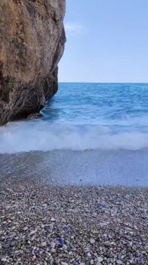 Kristal berrak turkuaz suyu ve kayalıklarla çevrili çakıl taşı plajı olan gizli bir koydan çarpıcı bir görüntü.