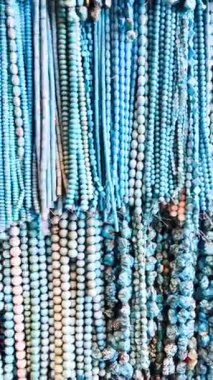 Yarı değerli taşlardan ve doğal malzemelerden yapılmış çok sayıda boncuk ve kolye yoğun sırada asılı, zengin ve renkli bir desen oluşturuyor..